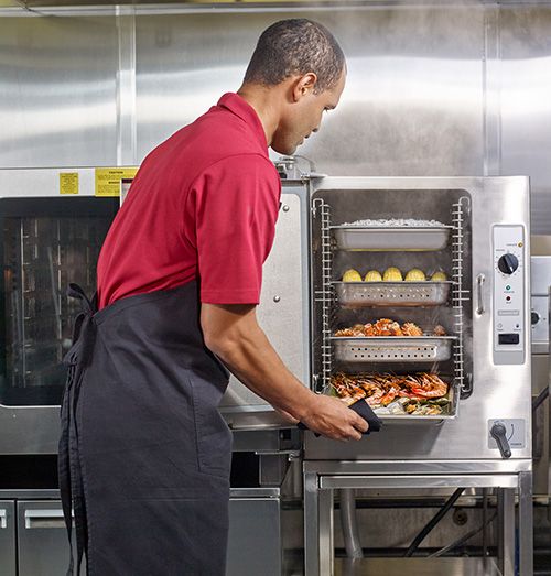 Cook wearing red shirt removing tray of seafood from 4 tray steamer