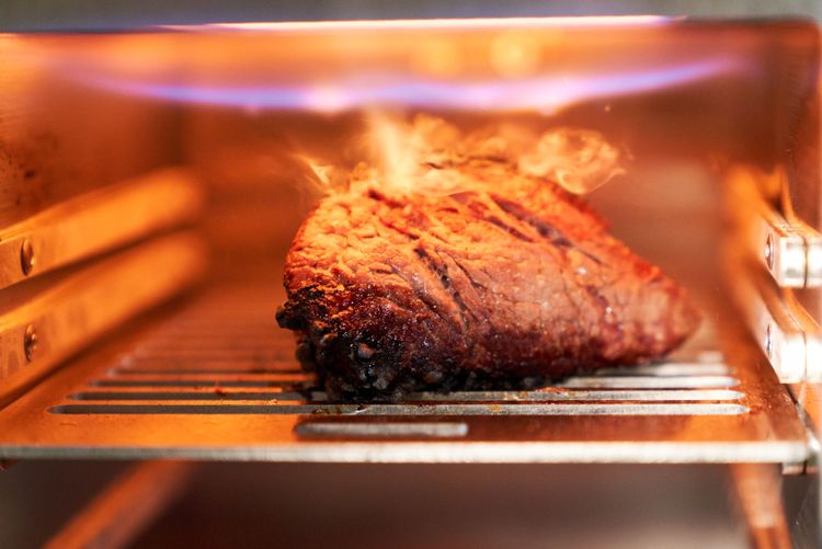 Meat cooking under the heat of a gas broiler