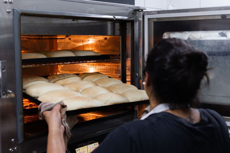 Female Baker removing a pan of perfectly baked golden brown rolls from the interior of a Convection oven.
