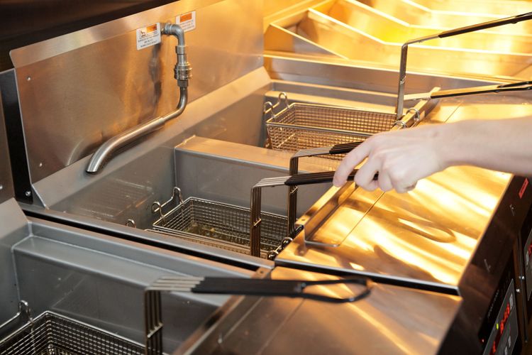 Fry cook holding fryer basked immersed in open pot fryer