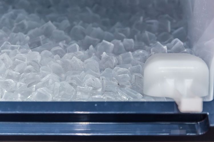 Interior of commerical ice maker with the bin filled with ice. White ice scoop is in the bin