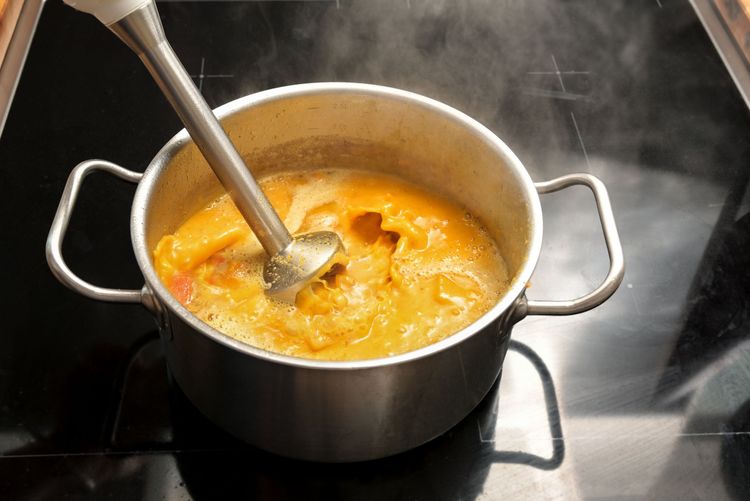 Stick Blender immersed in yellow liquid in a two handled stainless steel pot