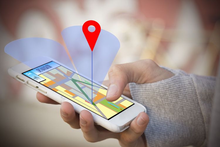 Person holding white cell phone in right hand while location icon hovers above the screen