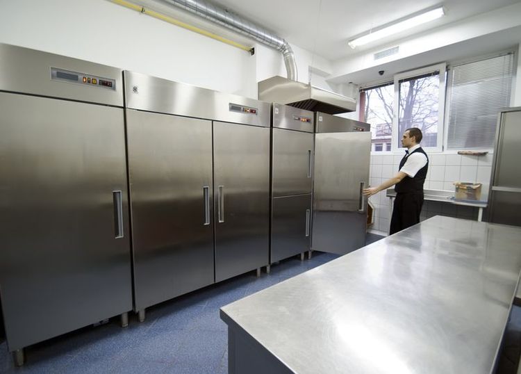 Waiter approaching a group of 3 large 2 door top compressor stainless steel reach ins