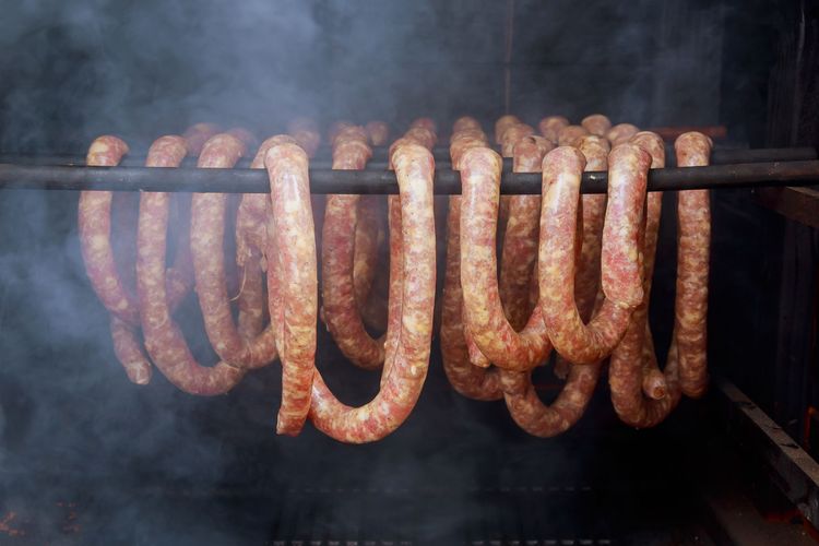 Rope sausage hanging from a rod in a smoker which smoke swirls around them