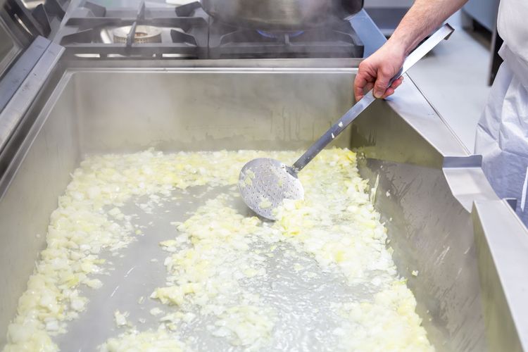 Chef stirring onions in a large tilt pan using a stainless steel kitchen tool to do so