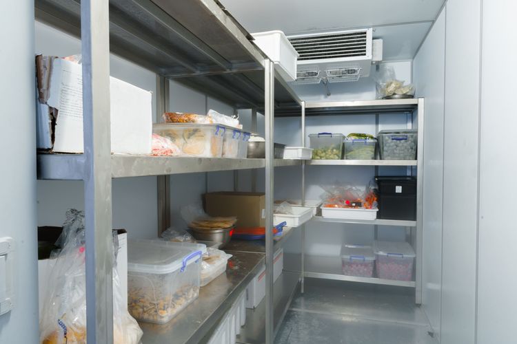 Brightly lit interior of walk in cooler with product well organized on beige plastic shelves